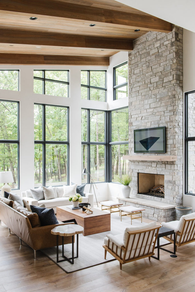 Modern Lakehouse by Studio McGee. Timeless interior design with large windows with black trim, wood floor and stone fireplace.  