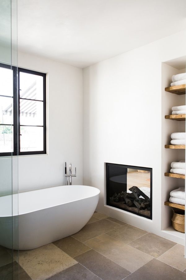Bathtub near window and fireplace with built-in wood shelves