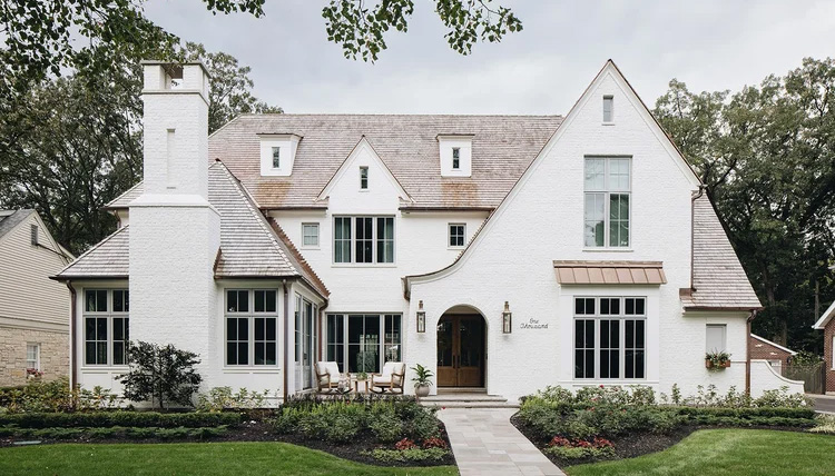 Large White home with Shake Shingles, steep gables and a sweeping roofline over an arched entry